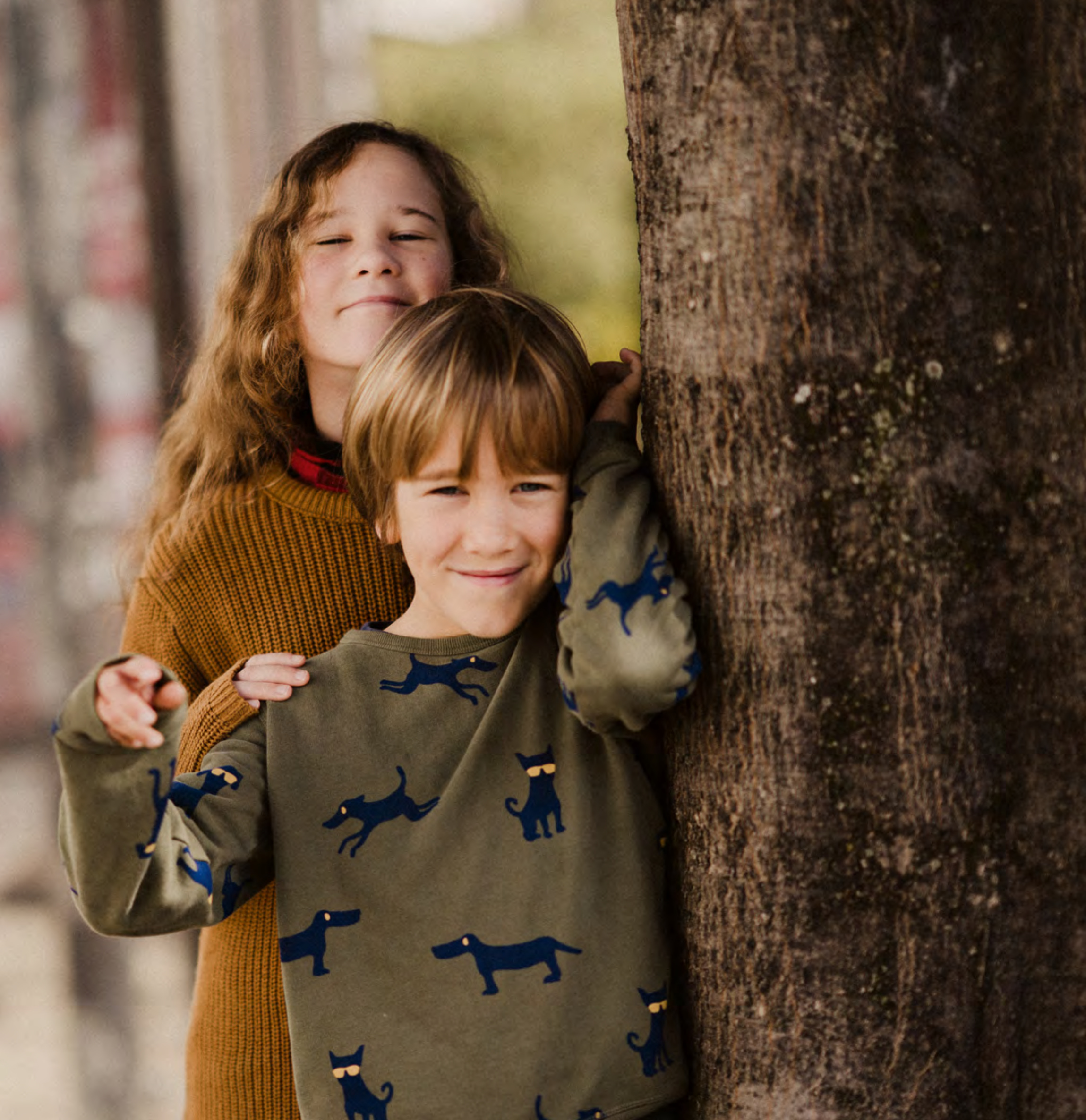 Zwei Kinder lehnen an einem Baumstamm